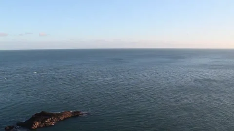 Panning from a clear sky down to a little rock island just off the coast Stock Footage 46006335