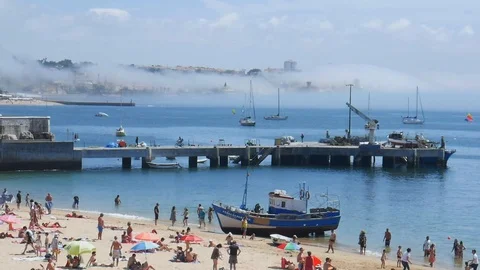 Panning of of crowded sandy Praia da Ribeira and boats on bay with thick fog in Stock Footage 113010523