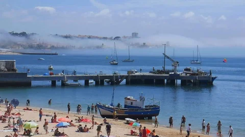 Panning of of crowded sandy Praia do Ribeiro and boats on bay with thick fog in Stock Footage 112998302