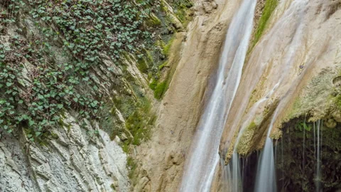 Panning down view of a waterfall surrounded by moss-covered stones 動画素材 150140204