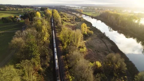 Panning drone shot overlooking the river while a train passes by during sunset Stock Footage 194446767