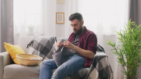 Panning of man sitting on sofa and knitting at cozy home Video stock 107349757
