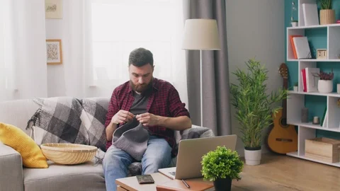 Panning of man sitting on sofa and watching knitting tutorial on laptop Video stock 107351063