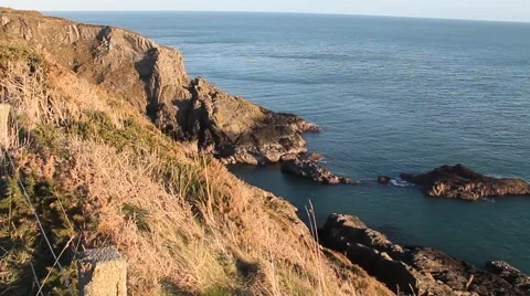 Panning from a mountain in sun down to a little rock island just off the coast Stock Footage 46006154