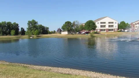 Panning shot of apartment complex pond with fountain on beautiful summer morning Stock Footage 201500570