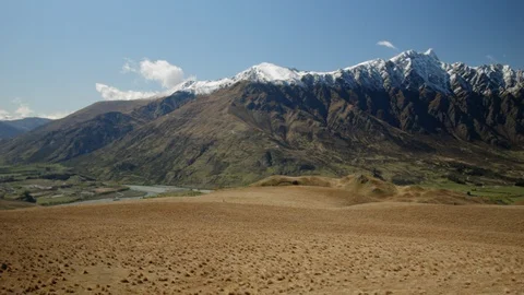 Panning shot of brown empty field with snow capped mountains, Queenstown Stock Footage 89572757