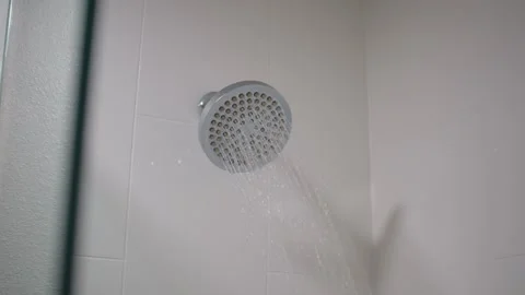 Panning shot of chrome shower head spraying water in a white tiled bathroom Stock Footage 329627560