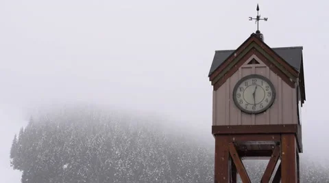 Panning Shot of Clock Tower With Mountain Backdrop and Snow Falling Stock Footage 57973306
