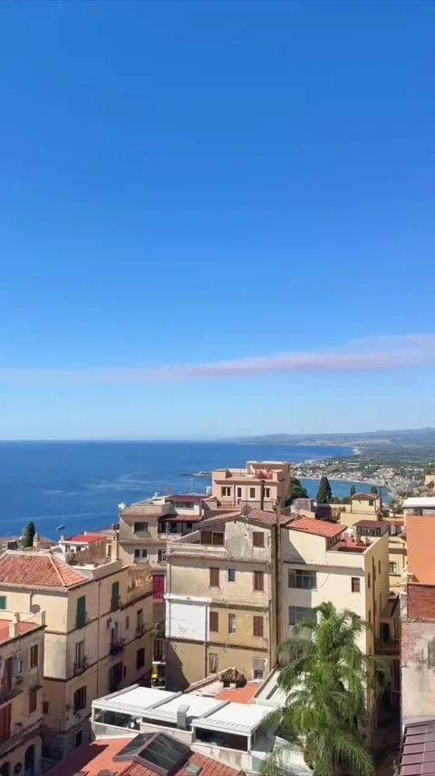 Panning shot of coastal town rooftops with distant smoking volcano under cl.. Stock Footage 346622461