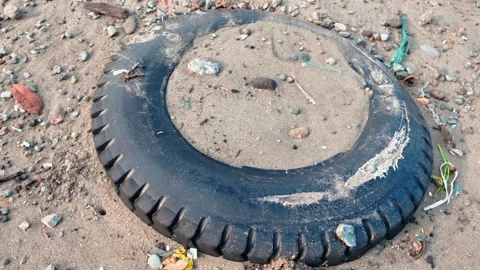 Panning shot of a discarded rubber tire buried in sand on a polluted beach. Stock Footage 337803401