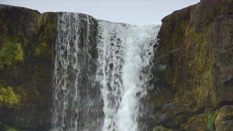 Panning shot down waterfall in Iceland, running over edge of mossy cliff Stock Footage 86754497