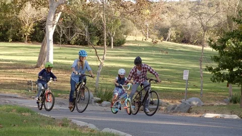 Panning shot following family cycling together in a park Stock Footage
