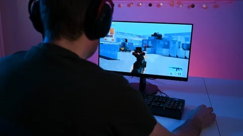 Panning shot of man with headset playing a first person shooter on pc Stock Footage 100722844