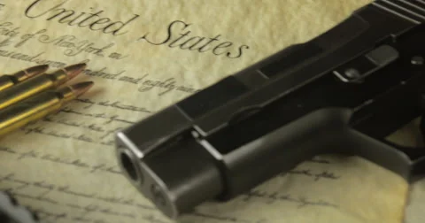 Panning Shot of Multiple Firearms and Ammunition Lying on the US Constitution Stock Footage 61280120