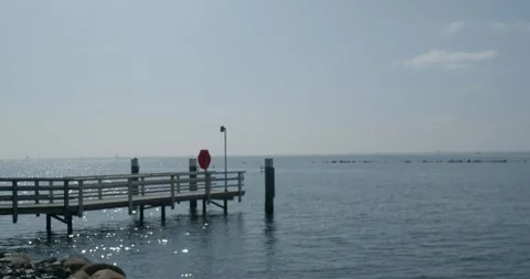 Panning shot small Fehmarn coastline pier to green energy wind turbines Stock Footage 286151798