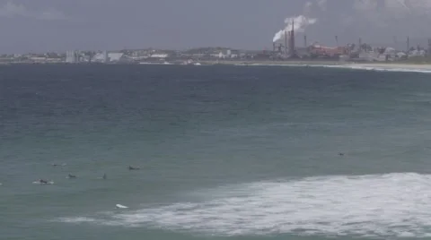 Panning shot of surfers waiting for waves in front of large factory. Stock Footage 56512726