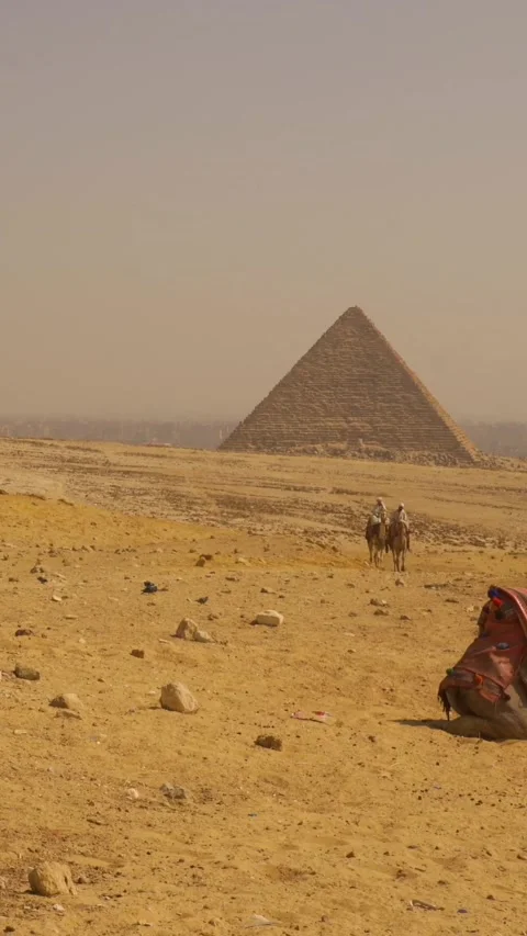 Panning shot of two local men riding a camel next to the Ginza pyramids Stock Footage 260472997