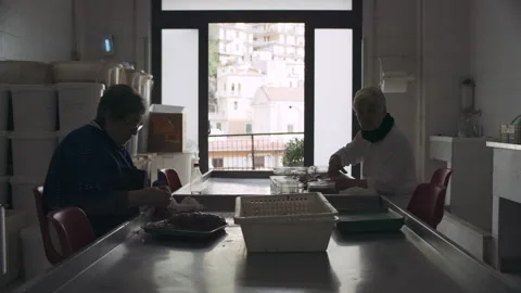Panning shot of two old cooks in an industrial kitchen preparing meat and other Stock Footage 199458038