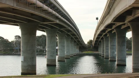 Panning shot underneath two bridges that cross a bay Vídeo Stock 121736767
