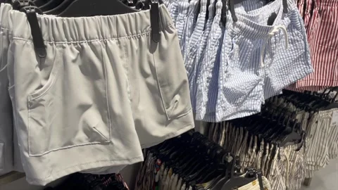 Panning shot of various casual summer shorts on hangers in a retail store. Vidéo 334324971