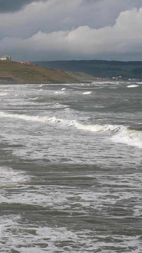 Panning shot of waves rolling in to the seaside town of Whitby Stock Footage 303780763