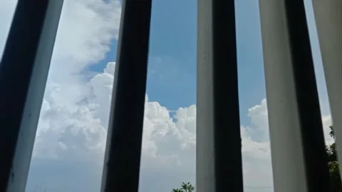 Panning shot of white clouds in blue sky behind window bars Stock-Footage 333484852