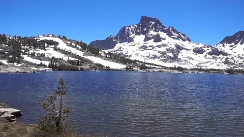 Panning view of alpine lake with snow covered mountains beyond Stockbeeldmateriaal 121503107