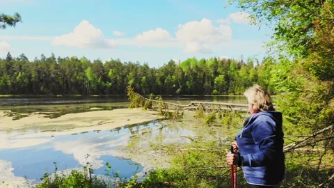 Panning view elderly blond caucasian woman stands holding red nordic sticks a Stock Footage 156204767