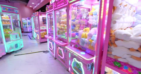Panning view of hall with many bright neon illuminated claw machines Stock Footage 319014665