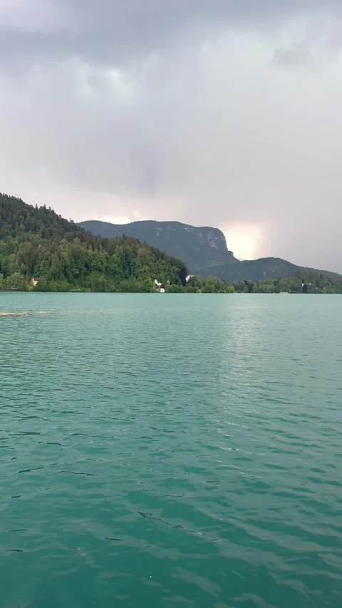 Panning view of Lake Bled with mountains and dramatic weather over water. The vi Stock Footage 337782128