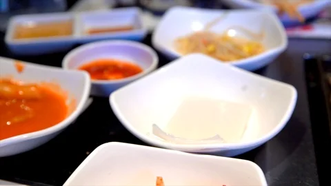 Panning view of side dishes and sizzling meat at korean bbq restaurant Stock Footage 96562326
