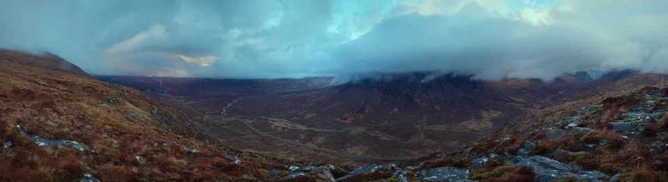 Panorama of a mountain range covered with clouds and a road in the valley Stock Photos