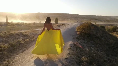 Panoramic back view of girl walking in a long yellow dress in the mountains of Stock Footage 221817388