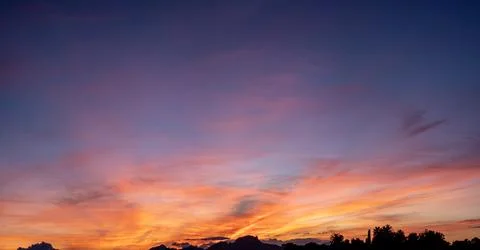 A panoramic dramatic sunset sky displaying rich gradients of deep blue, purpl Stock Photos