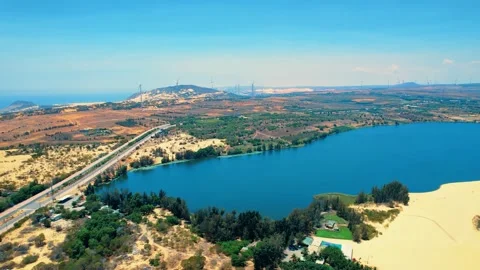 Panoramic drone flight over an emerald desert lake and distant wind farm 4K Stock Footage 338369432
