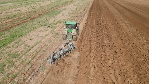 A panoramic drone view of a tractor plowing a vast Stock Footage 239834631