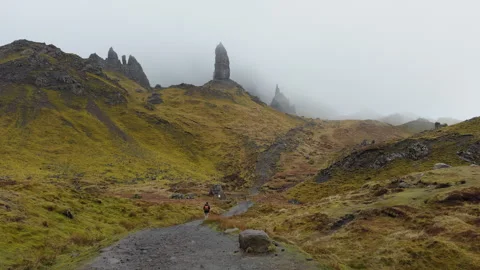 Panoramic ground shot of one person walking toward Old Man of Storr on a cloudy Vidéo 335163518