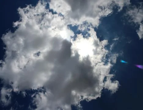 Panoramic image of the sun behind the clouds on the blue sky background. Stock Photos