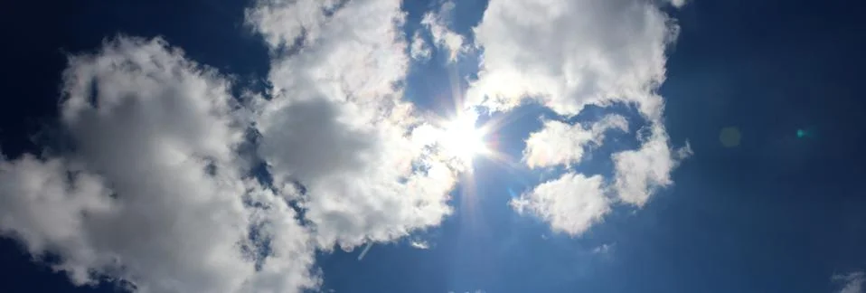 Panoramic image of the sun behind the clouds on the blue sky background. Foto stock
