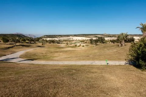 A panoramic landscape of a golf course with a golf cart path under clear blue Stock-Fotos