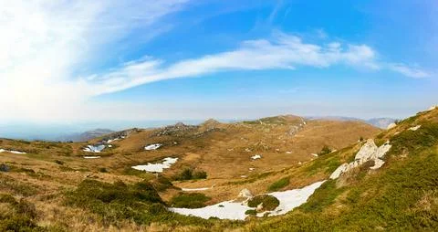Panoramic mountain valley with rocky cliffs and snow patches under blue sky Stock Photos