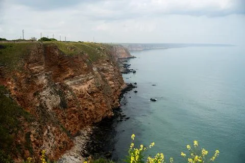 Panoramic red limestone cliffs stretching along calm sea under soft cloudy .. Stock Photos