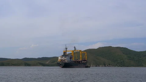 Panoramic shot of a cargo ship anchored near a deserted rocky coast, hills of Stock Footage 223004950