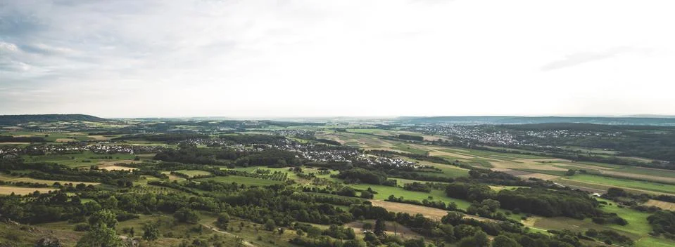 A panoramic shot of grassy fields with trees and buildings in the distance un Stock Photos