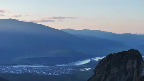 Panoramic valley at dusk with winding river, small town, and layered mountains 库存影片 345167501