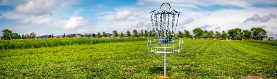 Panoramic view across an open grass disc golf course with a chain goal Stock Photos