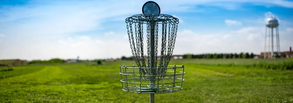 Panoramic view across an open grass disc golf course with a chain goal 스톡 사진