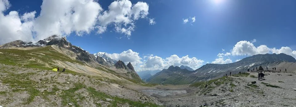 Panoramic View of Alpine Mountain Pass with Hikers, Tent and Snow Peaks Foto stock