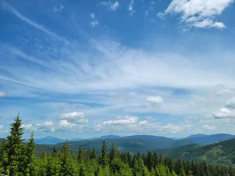 Panoramic view of clear blue sky, fluffy clouds, mountains, and trees. Stock Photos