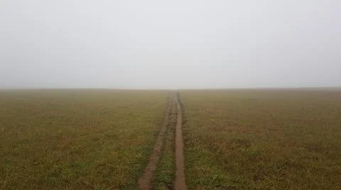 Panoramic view of the dirt road through the field in the fog at dawn. Europe Stock Photos